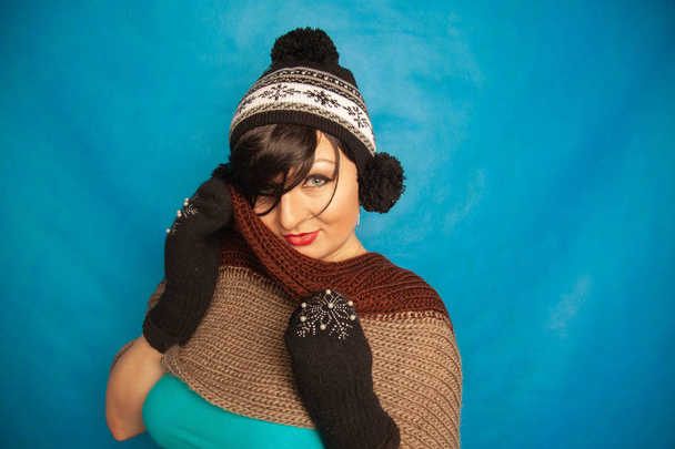 красивая брюнетка девушка в моде черные вязаные зимние шляпы и теплые красивые варежки на синем студийном твердом фоне
 - Фото, изображение