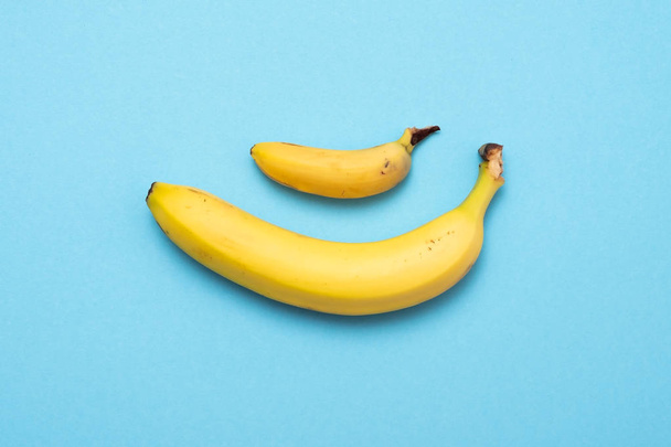 Malý banán porovnání velikosti s banánem na modrém pozadí. velikost penisu koncept - Fotografie, Obrázek
