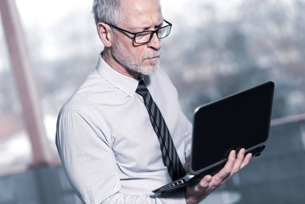 Senior businessman standing and working on his laptop - Фото, зображення