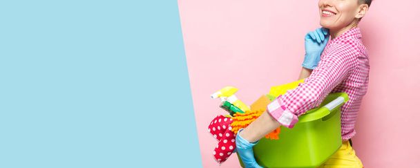 Giovane donna con attrezzi e prodotti per la pulizia in secchio, isolata su rosa e blu
 - Foto, immagini