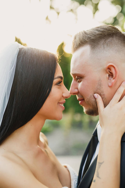 young beautiful wedding couple bride and groom are standing in the park at sunset and smiling bride in beautiful dress groom is dressed stylishly - Zdjęcie, obraz