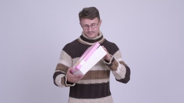 Happy bearded man thinking while holding gift box - Кадры, видео