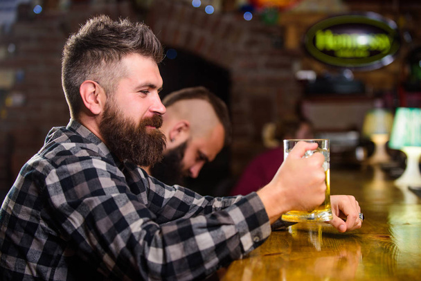 Man with beard spend leisure in dark bar. Brutal hipster bearded man sit at bar counter drink beer. Order alcohol drink. Bar is relaxing place have drink and relax. Hipster relaxing at bar with beer - Foto, Imagen