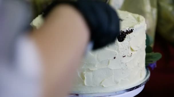 Konditor Hand in Hand in schwarzem Handschuh schneidet großen Schokoladenkuchen mit weißer Sahne mit dem Messer und verschenkt eine Scheibe - Filmmaterial, Video