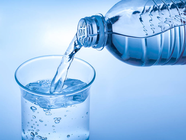 Verter agua cristalina de la botella sobre vidrio sobre fondo azul
 - Foto, imagen