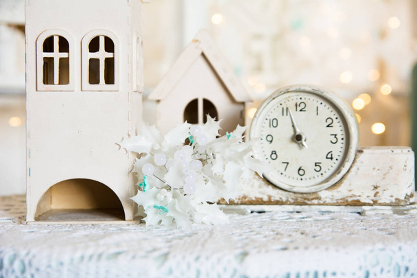 An alarm clock is on a table with toy house and flower decoration. - Foto, Imagen