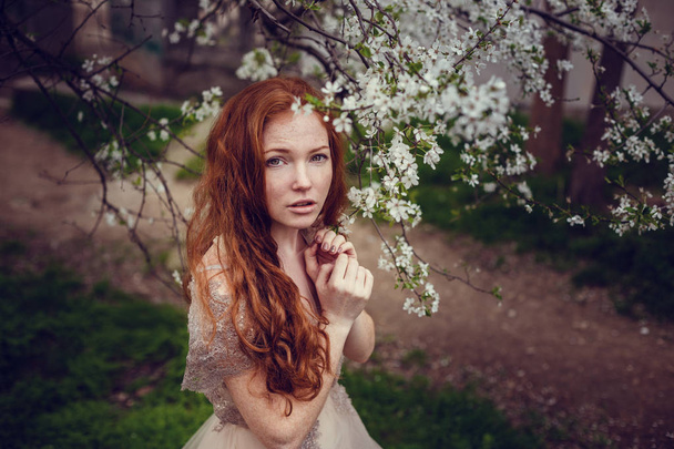 Hermosa joven feliz con el pelo rojo disfrutando del olor en un jardín de primavera floreciente
. - Foto, imagen