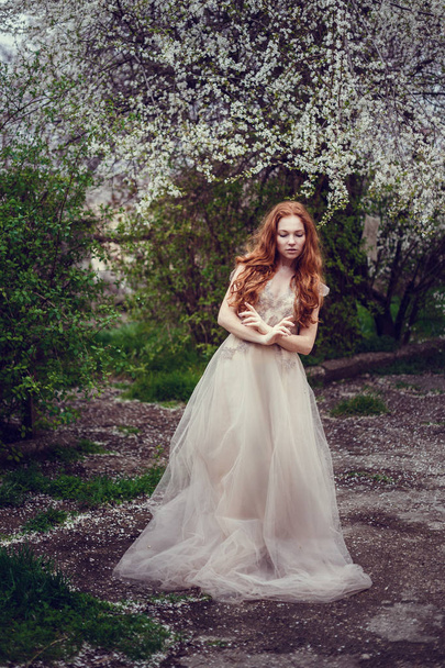 Hermosa joven feliz con el pelo rojo disfrutando del olor en un jardín de primavera floreciente
. - Foto, imagen