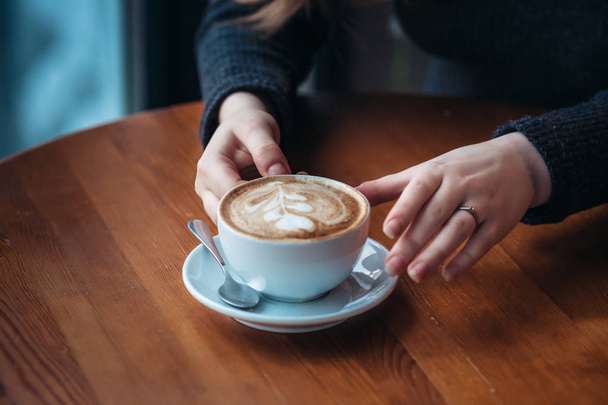 Beautiful young woman enjoying coffee cappuccino with foam near window in a cafe - Foto, afbeelding