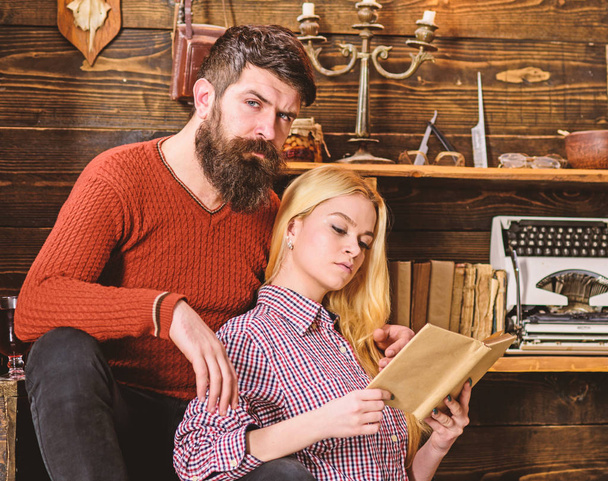 Couple in love reading poetry in warm atmosphere. Lady and man with beard on dreamy faces with book, reading romantic poetry. Couple in wooden vintage interior enjoy poetry. Romantic evening concept - Photo, image