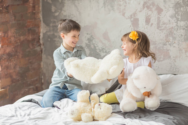 Brother and sister playing with teddy bear in bed - Foto, afbeelding