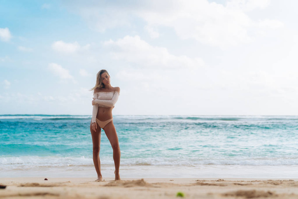 Mooi gelooid meisje permanent op strand met wit zand en blauwe oceaan - Foto, afbeelding