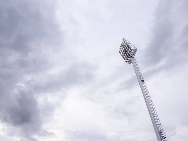 Нижний вид на один высокий столп прожекторов, который окружен белым и облачным небом. Монотон
. - Фото, изображение