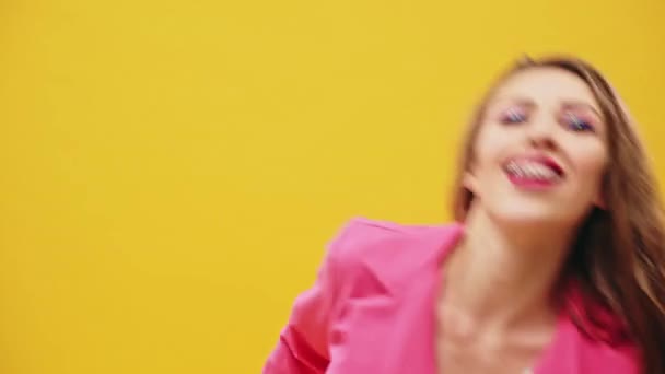 Pretty young female with bright makeup smiling and looking at camera while dancing actively on yellow background - Filmagem, Vídeo