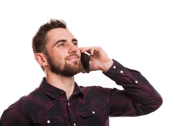 Close up portrait of a handsome bearded man talking on the phone, looking away happily, isolated. Attractive man smiling, calling using his smart phone, copy space. Technology, communication concept - Fotó, kép