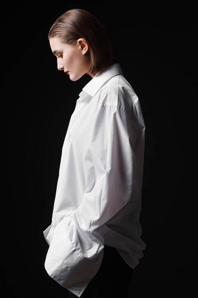 Portrait of an elegant young woman in a white shirt and black pants. Interesting studio light - Zdjęcie, obraz