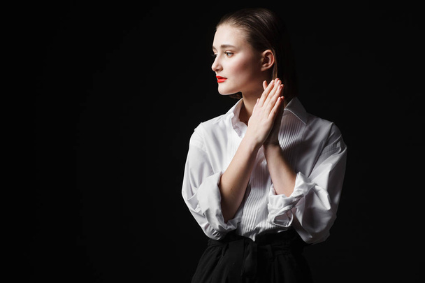 Portrait of an elegant young woman in a white shirt and black pants. Interesting studio light - Foto, afbeelding