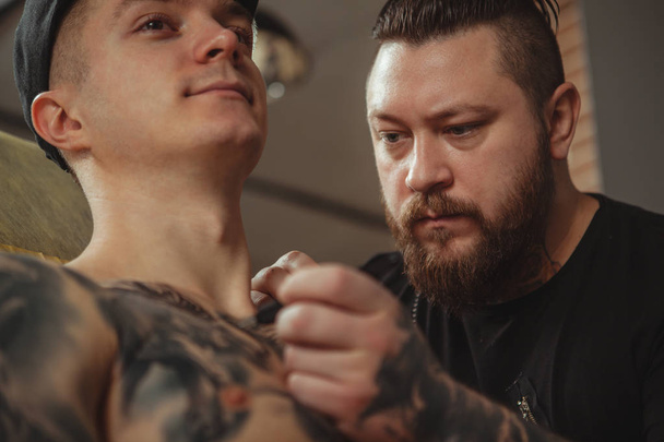 Tattoo artist working with his client at art studio - 写真・画像