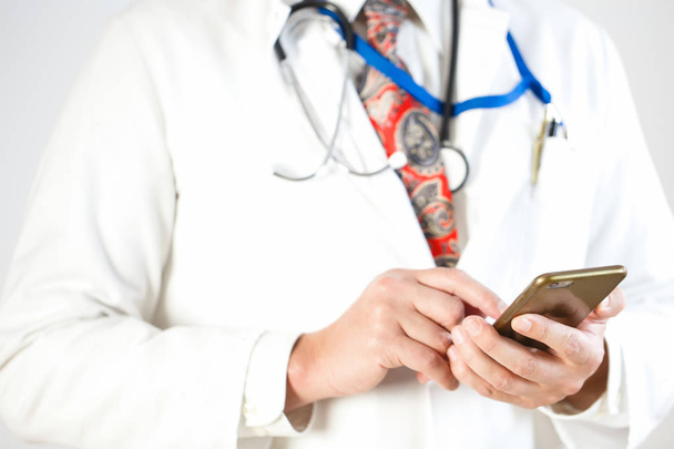 Ένας γιατρός σε ισοπαλία και με ένα στηθοσκόπιο κρατάει ένα smartphone. - Φωτογραφία, εικόνα