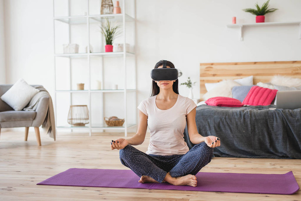 Young female doing yoga in VR glasses at home - Fotoğraf, Görsel