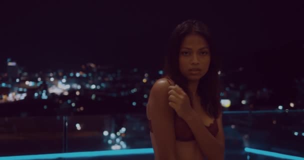 Beautiful woman in red lingerie looking into the camera while sitting on the yellow sofa over city landscape at night - vide in slow motion - Footage, Video