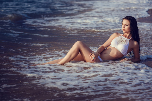schattig en sexy meisje in bikini genieten van zomer. Outdoor Portret. Zee golven en witte schuim. Zonsondergang na de regen op het eiland - Foto, afbeelding