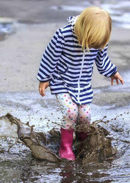Niño juguetón al aire libre saltar en el charco en la bota después de la lluvia - Foto, imagen