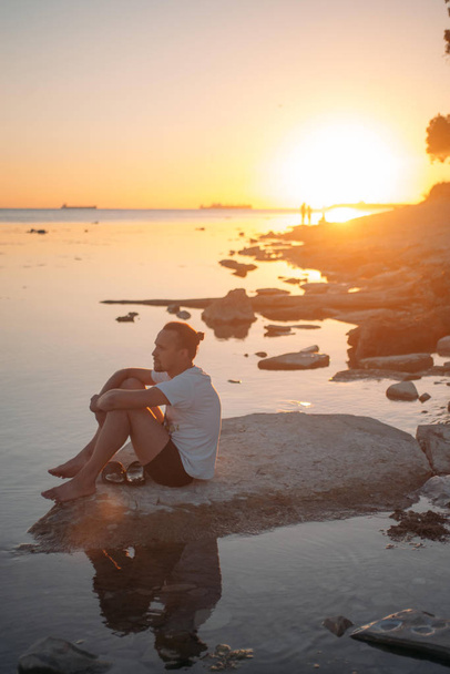 Un joven sentado en una piedra junto al mar
.  - Foto, imagen