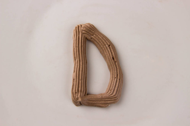 Шоколадная буква D, нарисованная со взбитыми сливками на белой тарелке
 - Фото, изображение