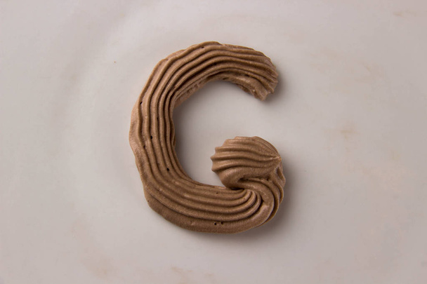 Zoete chocolade letter G getekend met slagroom op een witte plaat - Foto, afbeelding