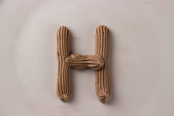 Солодкий шоколадний лист H намальований зі збитими вершками на білій тарілці
 - Фото, зображення