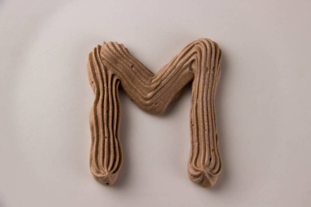 Dolce lettera M al cioccolato disegnata con panna montata su un piatto bianco
 - Foto, immagini