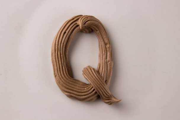 Шоколадная буква Q нарисованная со взбитыми сливками на белой тарелке
 - Фото, изображение