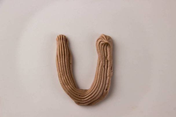 Сладкая шоколадная буква U нарисованная со взбитыми сливками на белой тарелке
 - Фото, изображение