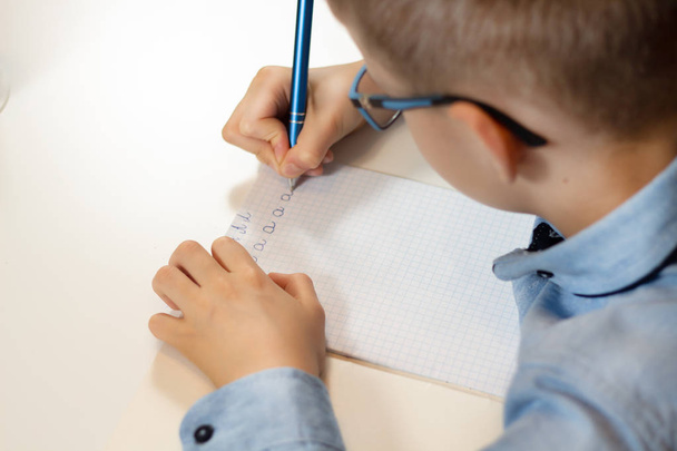 少年は彼の手にペンで机に座って、ノートに書き込みます。子書くことを学ぶ。少年の手はペンを持っています。リットルをノートに書く. - 写真・画像