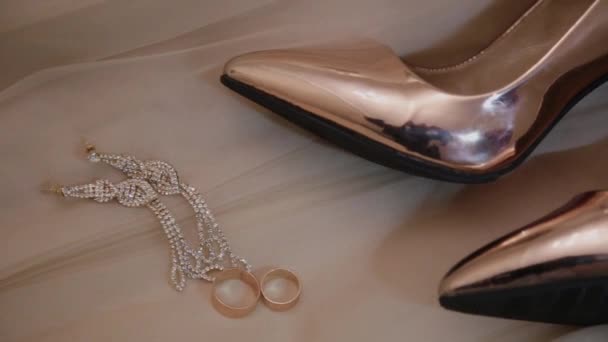 arany női esküvői cipők, gyűrűk és ékszerek az ágyon. - Felvétel, videó