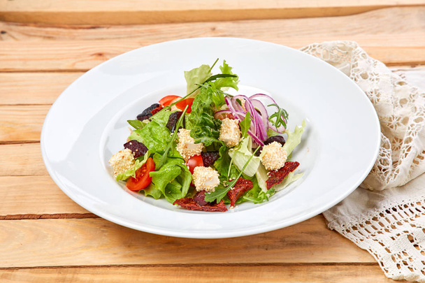 вегетарианский салат с сушеными помидорами и гренками на белой тарелке, крупным планом
  - Фото, изображение