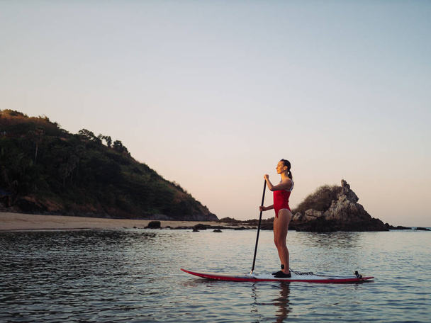 Donna in costume da bagno rosso su SUP stand up paddle board su una baia al tramonto
 - Foto, immagini