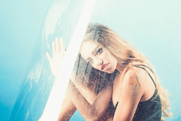 Shower and hygiene spa treatment. Sexy woman behind plastic sheet with water drops. Fashion and beauty. Rain drops on window glass with face of girl. Window with water drops before girl with makeup - Valokuva, kuva