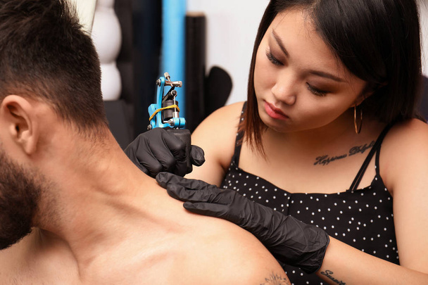 Professional artist making tattoo with machine in salon - Fotó, kép