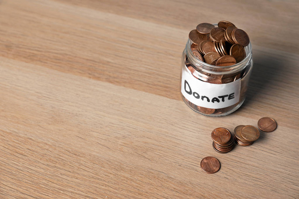 Glass jar with money and label DONATE on wooden background. Space for text - 写真・画像