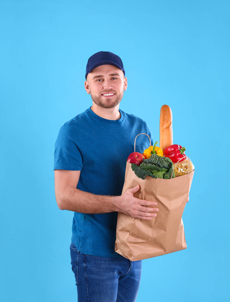 Delivery man holding paper bag with food products on color background - Zdjęcie, obraz