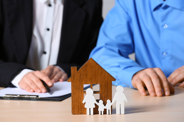 Real estate agent working with client at table, focus on house and family figures. Home insurance - Фото, зображення
