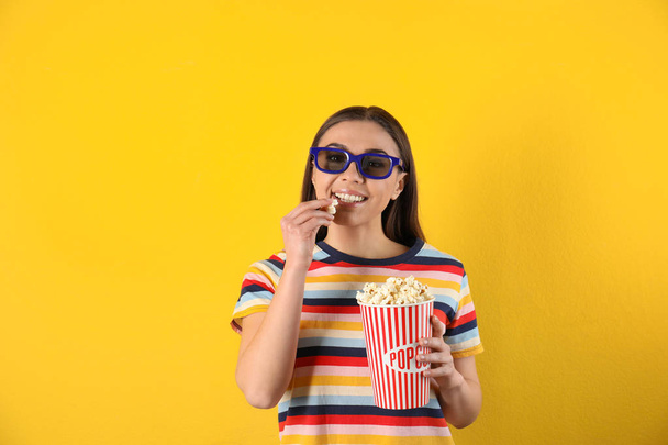 Jonge vrouw met 3D-bril en lekkere popcorn op kleur achtergrond - Foto, afbeelding