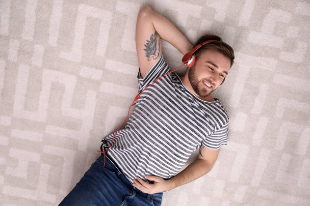 Young man in headphones enjoying music on floor, top view - Photo, Image
