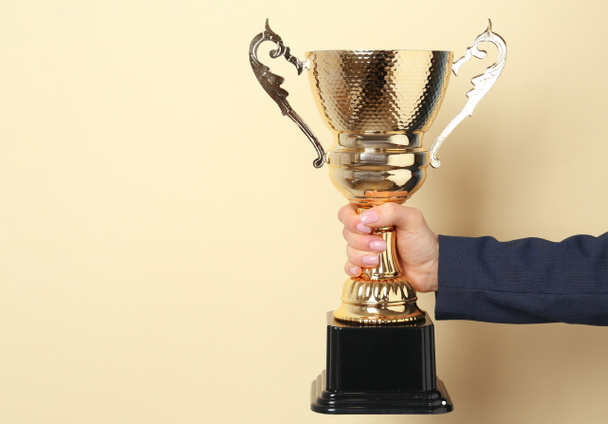 Woman holding golden trophy cup on color background, closeup. Space for text - Photo, Image