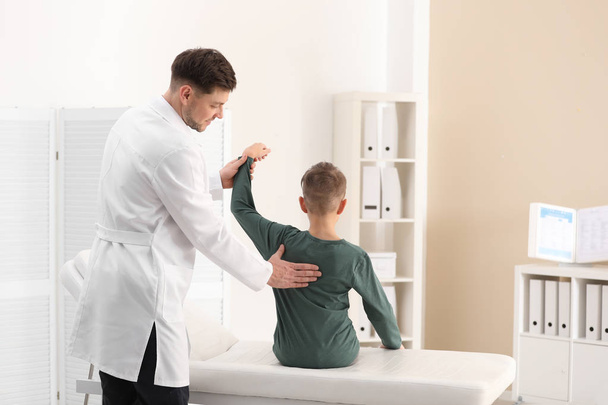 Chiropractor examining child with back pain in clinic - Foto, afbeelding