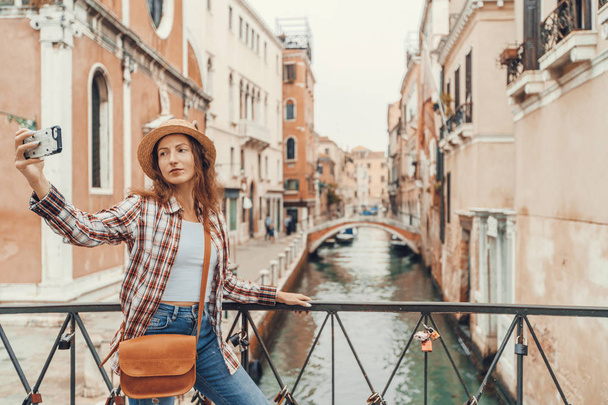 Женщина делает селфи со смартфоном в Венеции. Путешественница, делающая автопортрет на венецианском мосту с красивым пейзажем на заднем плане, Венице, Италия
. - Фото, изображение