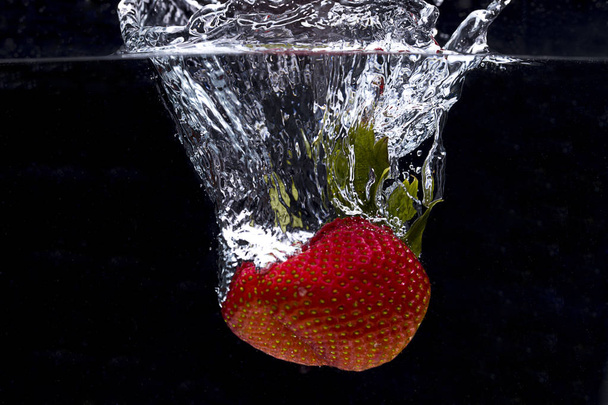 Large strawberry dropped in water. - 写真・画像