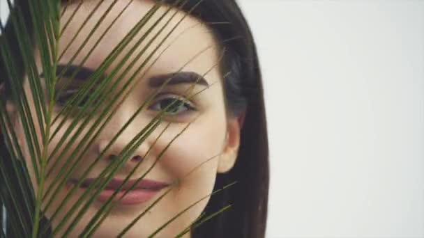 Young beautiful smiling model with natural makeup, long eyelashes and green leaf of ferns. Spa, skin care and wellness. Beauty and Skin Care Concepts. - Materiał filmowy, wideo